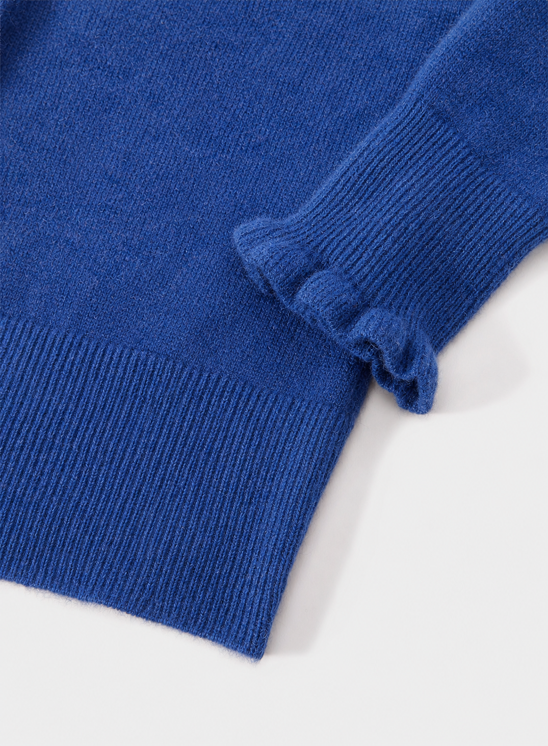 A close-up of a royal blue ribbed knit garment, showing the texture and ruffled cuff detail against a clean white background.