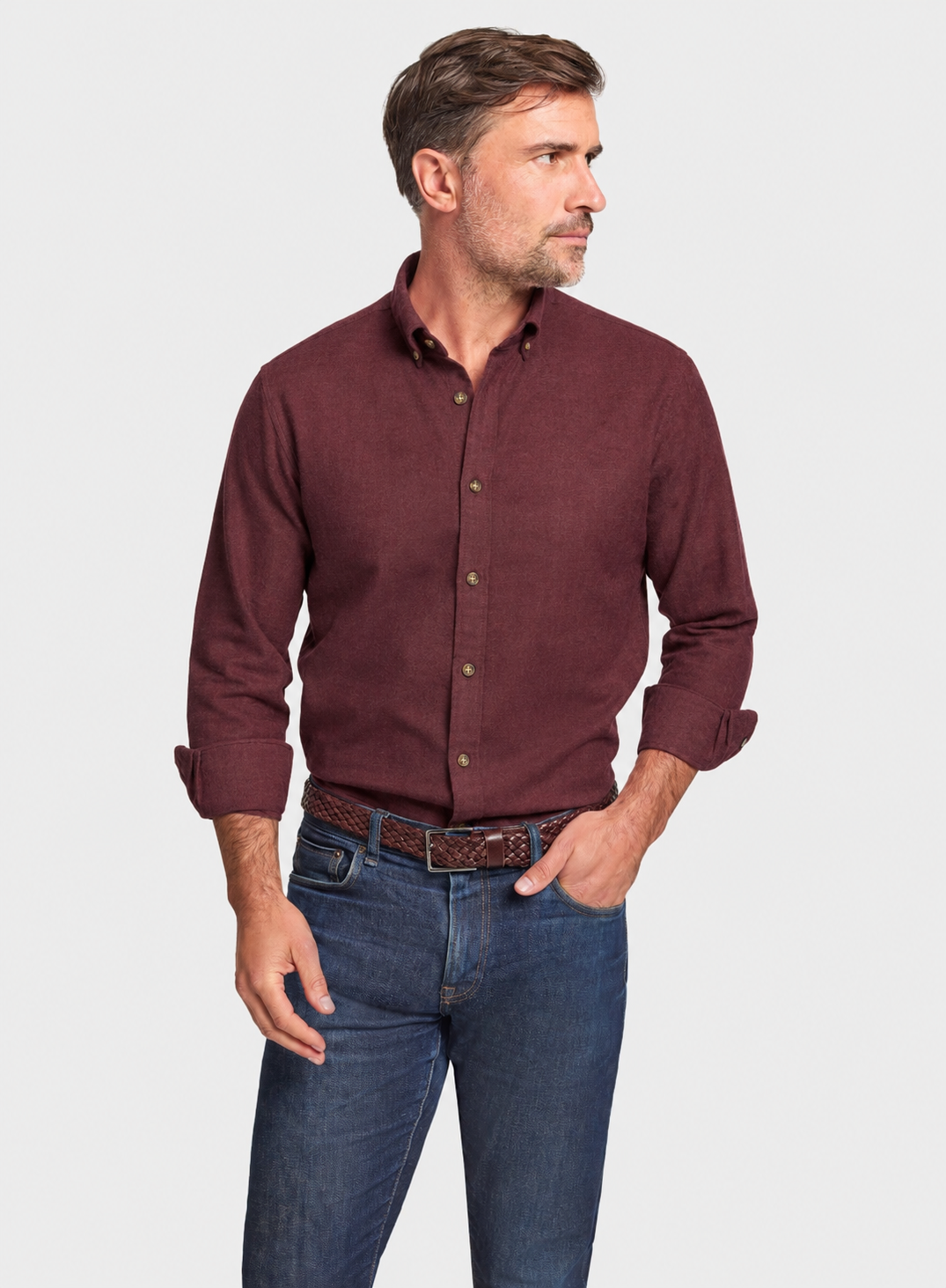 A man wearing a long-sleeve button-down shirt in maroon and blue jeans, standing against a light gray background.