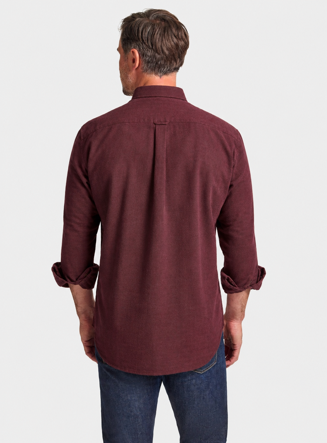 A man viewed from the back wearing a maroon long-sleeve button-down shirt with rolled-up sleeves and blue jeans, set against a plain light gray background.