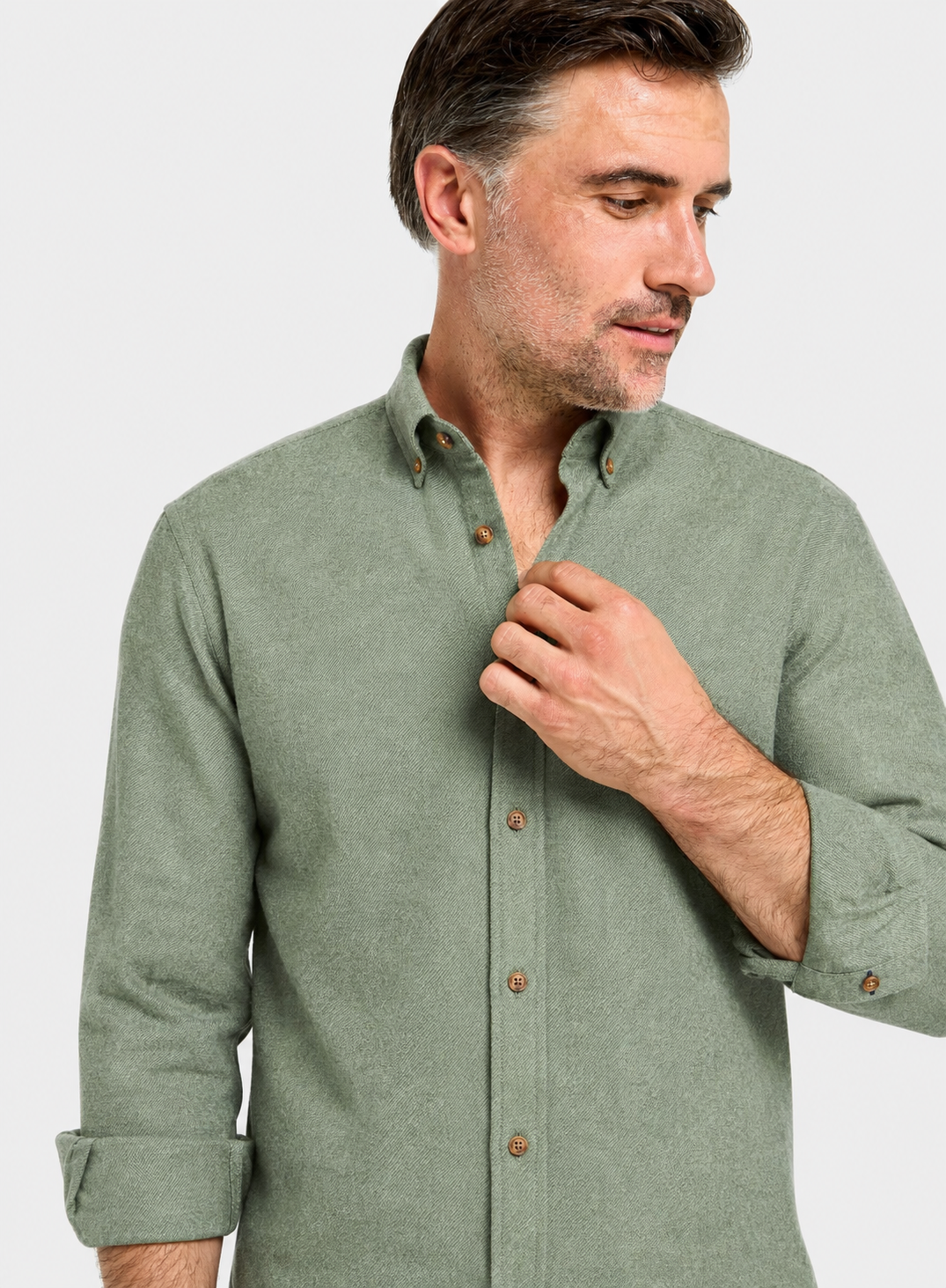 A man wearing a sage green long-sleeve button-down shirt, shown from the chest up against a light gray studio background.