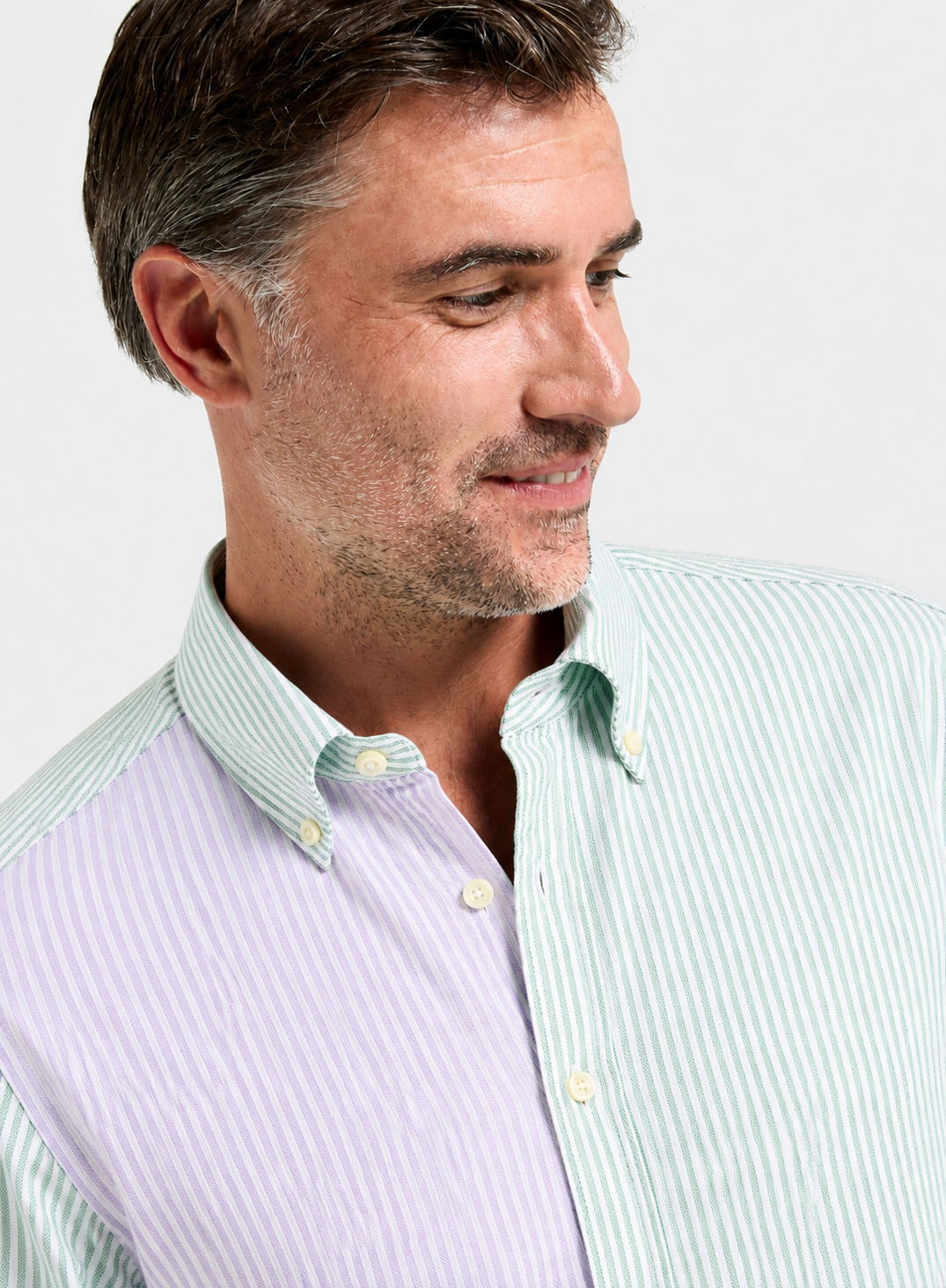 A close-up of a man wearing a button-down shirt with a dual-panel design: one side is mint green and white striped, and the other side is lavender and white striped.