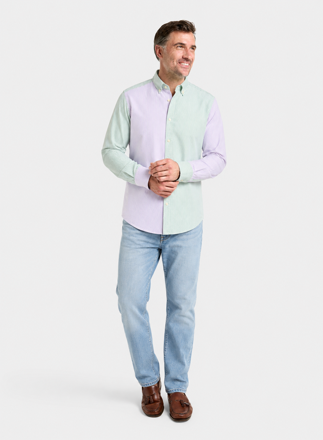 A man wearing a long-sleeve button-down shirt with a split color-block design in pale mint green and light lavender, paired with light blue jeans and brown leather loafers, standing against a light gray studio background.