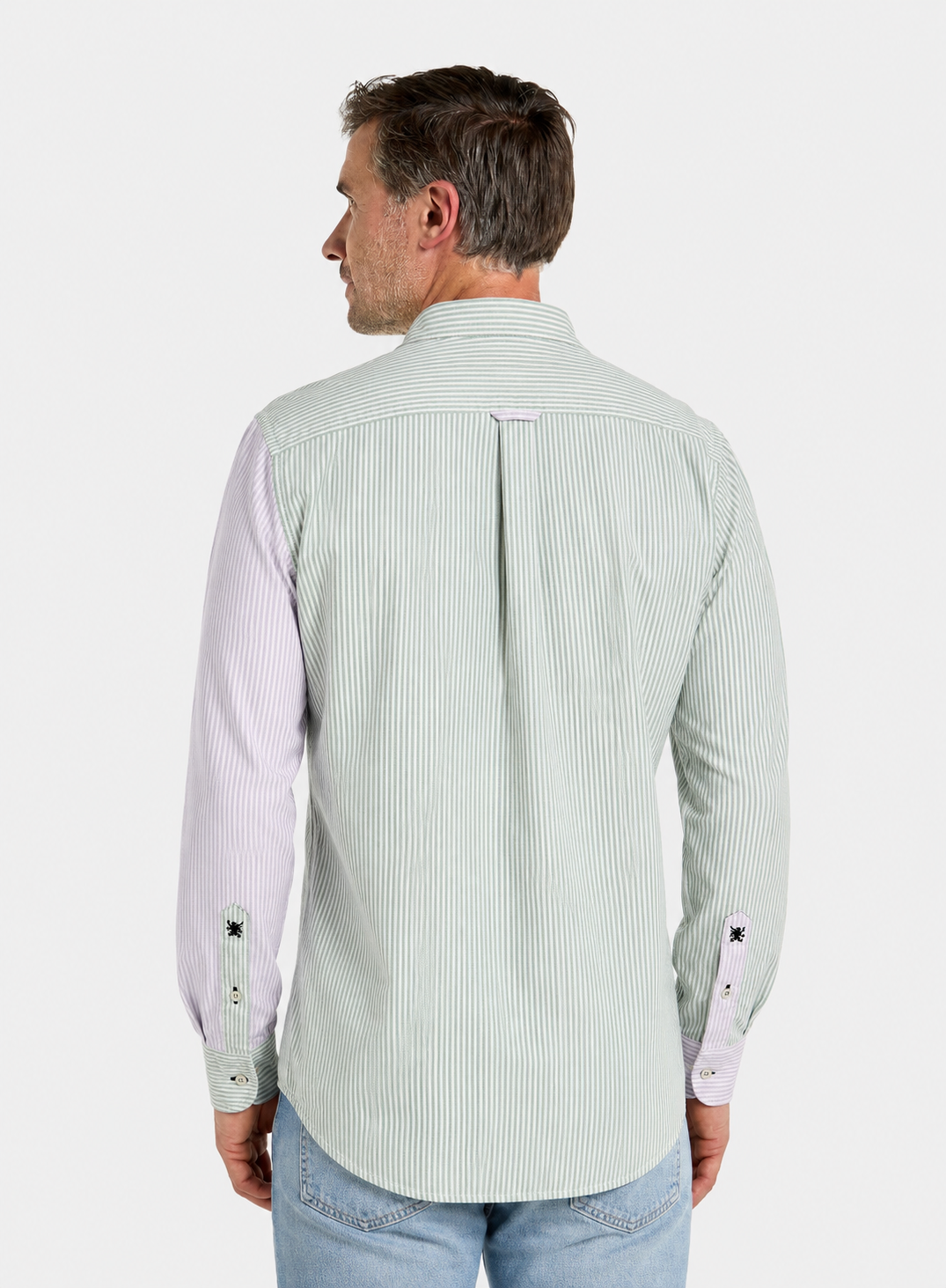 A man viewed from the back wearing a light green and white vertically striped long-sleeve shirt with contrasting pale pink sleeves, paired with light blue jeans, against a plain light gray background.
