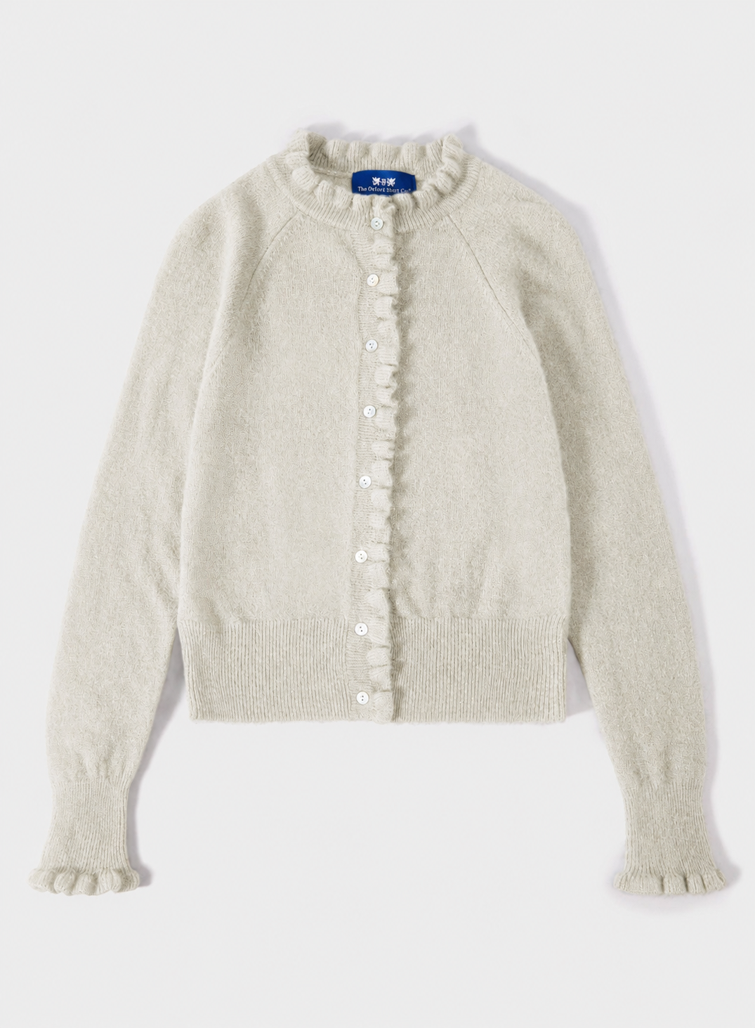 A cream-colored knit cardigan sweater with ruffle trim along the front button placket and cuffs, shown flat on a light gray background.