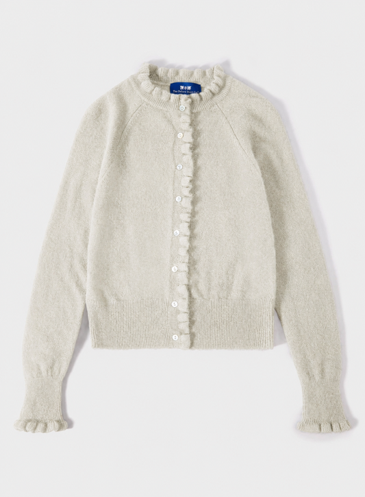 A cream-colored knit cardigan sweater with ruffle trim along the front button placket and cuffs, shown flat on a light gray background.