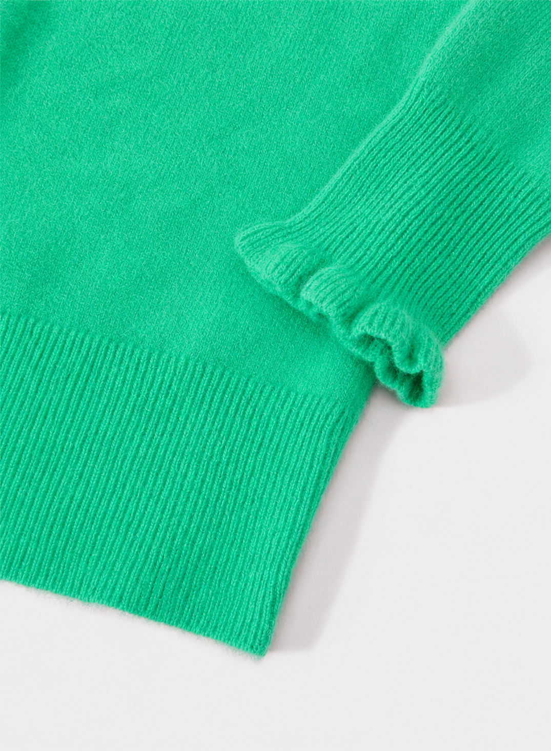 Close-up of a bright green ribbed knit garment, showing the sleeve cuff with a ruffled edge and the main body fabric on a light background.