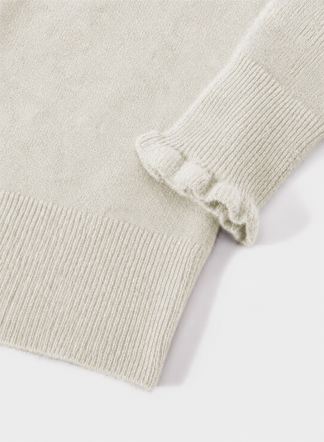 Close-up of a light beige knit sweater showing the ribbed cuff and sleeve with a ruffled edge detail, on a white background.