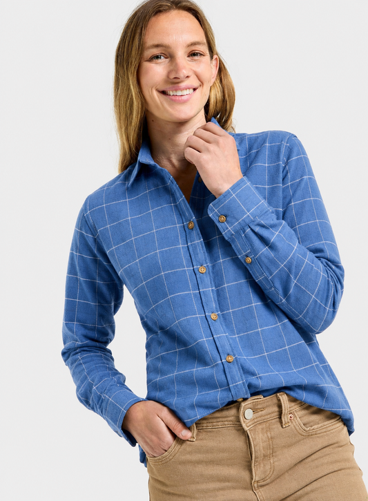 A woman wearing a blue long-sleeve button-up shirt with a white windowpane plaid pattern and tan pants, posing against a light gray studio background.