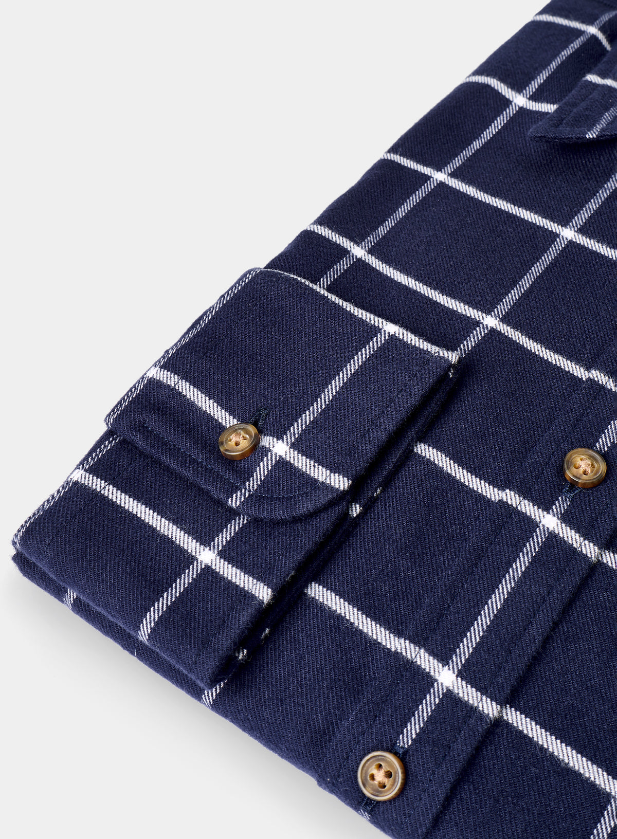 Close-up of a navy blue shirt with white check pattern and gold buttons on a light gray background
