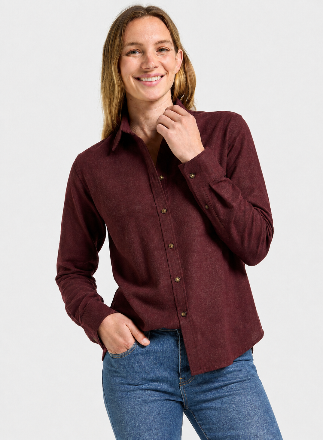 A woman wearing a long-sleeve button-up shirt in maroon and blue jeans, standing against a light gray studio background.