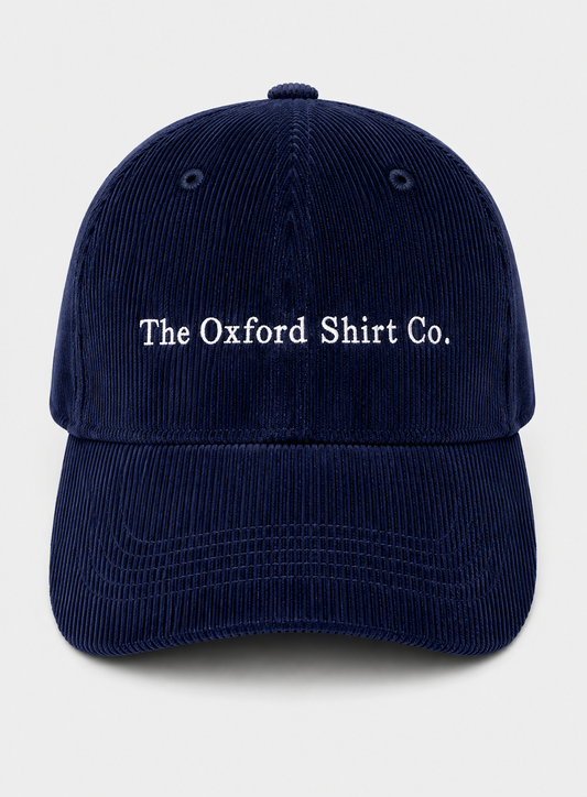 A navy blue corduroy baseball cap with 'The Oxford Shirt Co.' embroidered in white on the front, set against a light gray background.