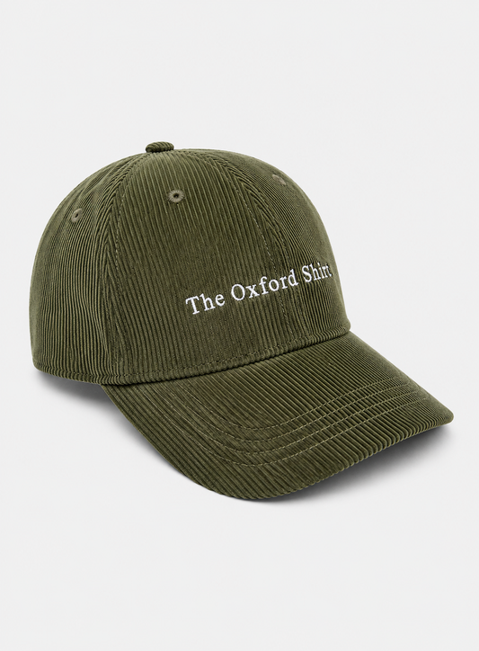 An olive green corduroy baseball cap with 'The Oxford Shirt' embroidered in white on the front, set against a light gray background.