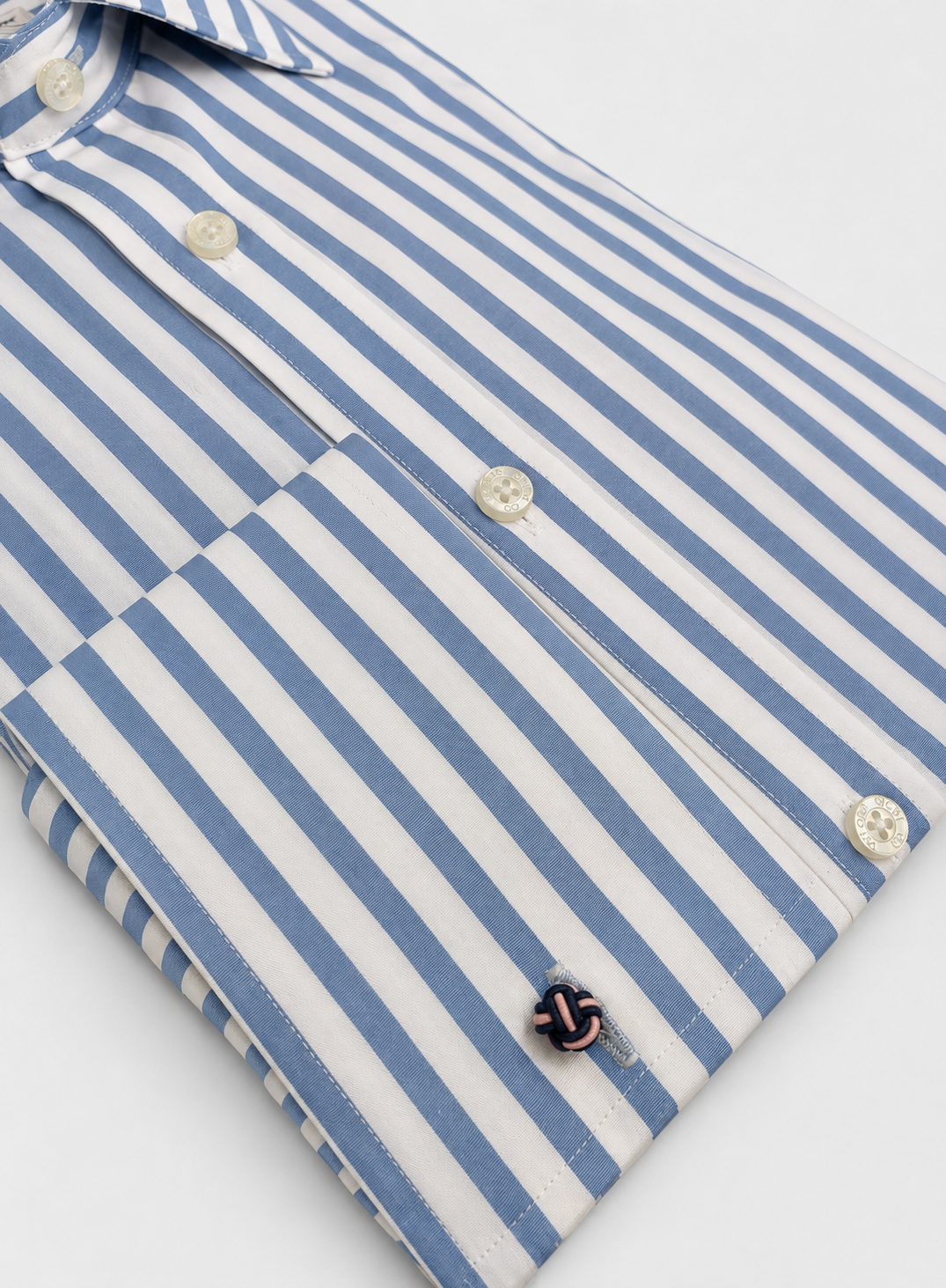 A close-up of a folded dress shirt with vertical blue and white stripes, featuring white buttons and a small embroidered cufflink.
