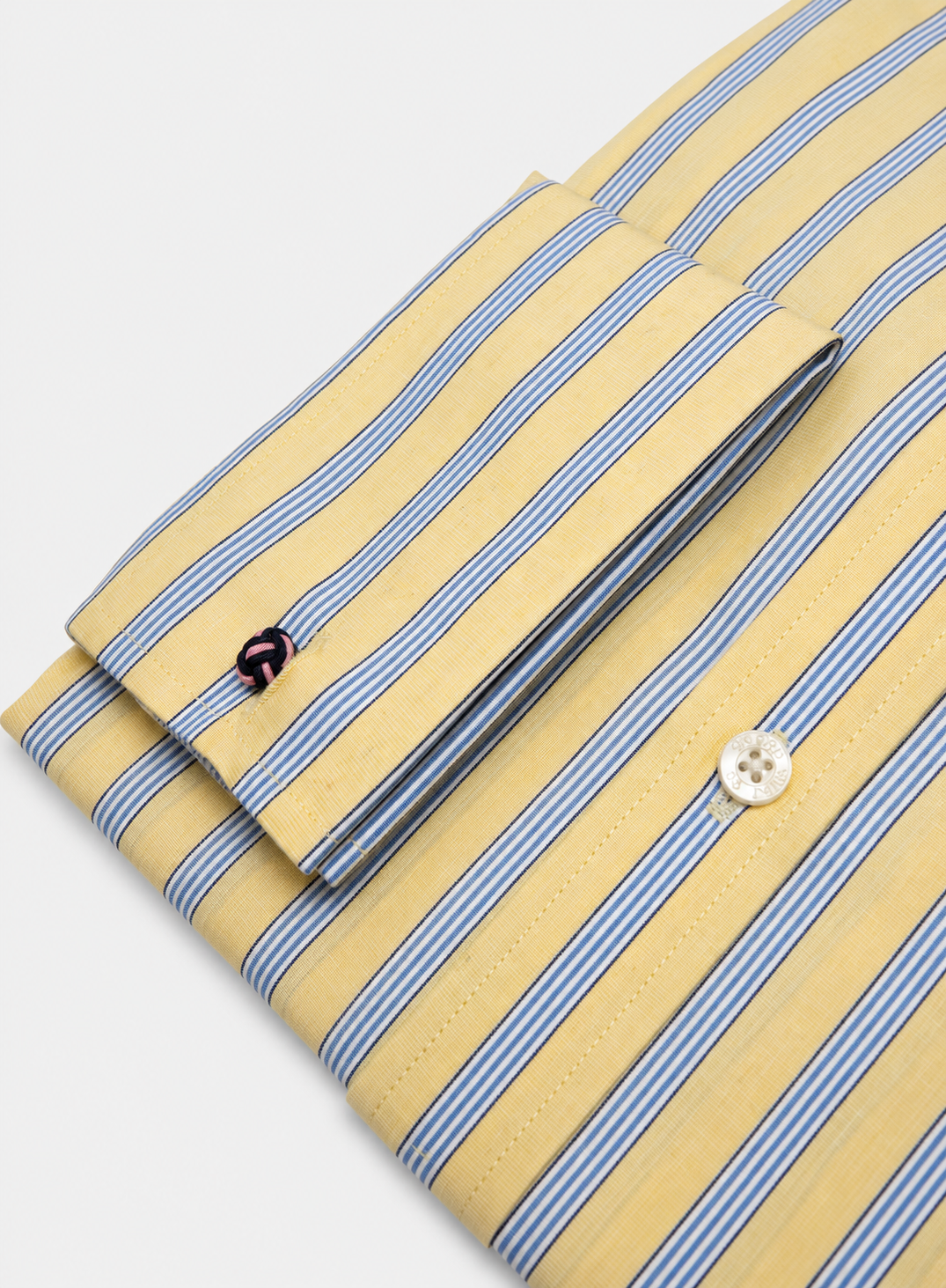 A folded long-sleeve dress shirt with a yellow base and thin blue and white vertical stripes, featuring a buttoned cuff and a white button.