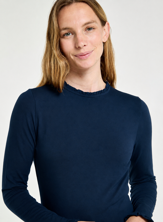 A woman wearing a dark navy blue long-sleeve crewneck top, photographed against a clean light gray studio background.