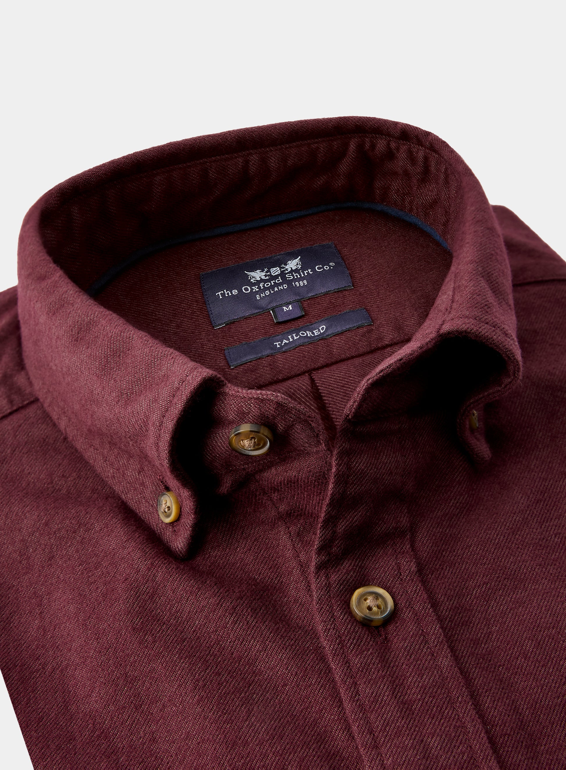 Close-up of a maroon shirt with a brand label on a white background