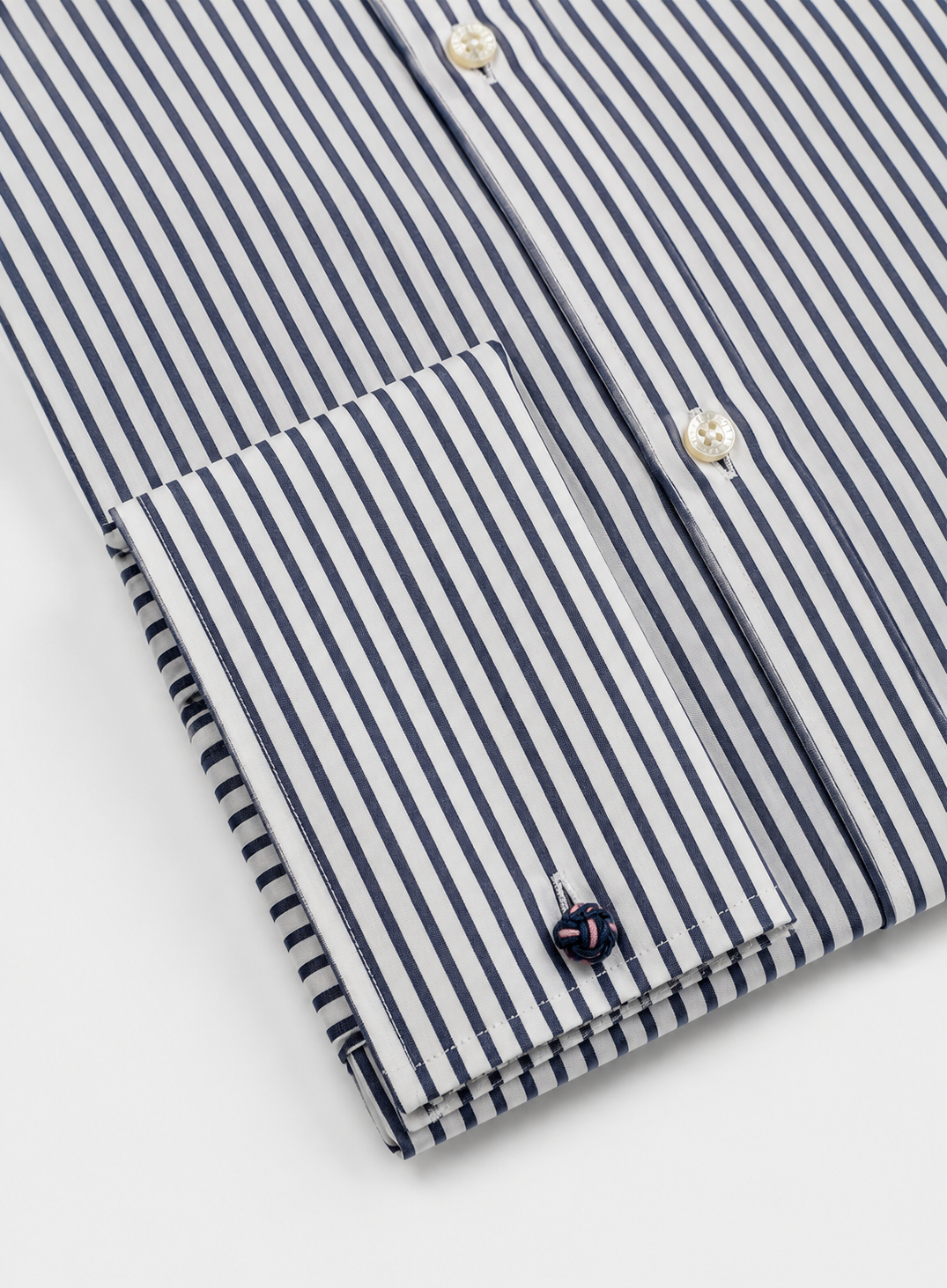 Close-up of a striped dress shirt with navy and white vertical stripes, featuring a button-down front, a single-button cuff, and a small embroidered logo on the cufflink.