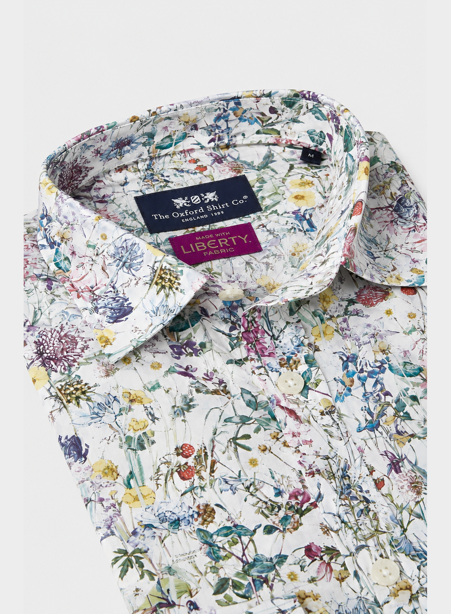 A close-up of a Liberty of London dress shirt by The Oxford Shirt Co., featuring a dense multicolor wildflower print on a white background.