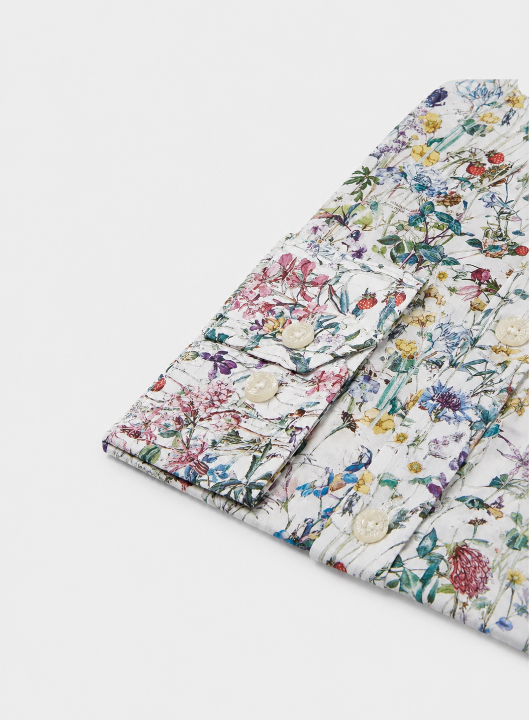 A folded shirt with a dense multicolor floral and botanical print on a white background, featuring decorative cream buttons on the cuff.